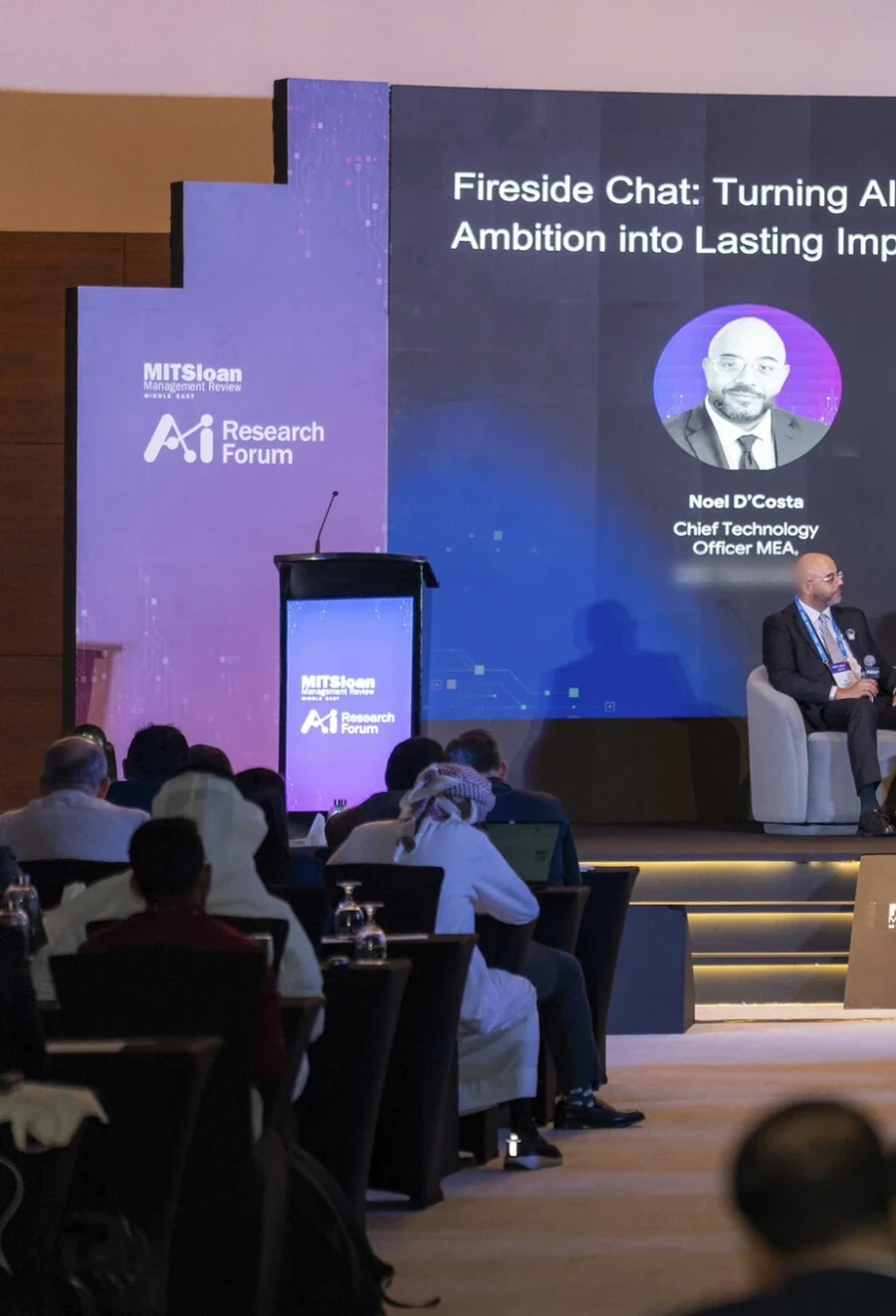 Noel D'Costa on stage at a fireside chat on AI, with the audience in front
